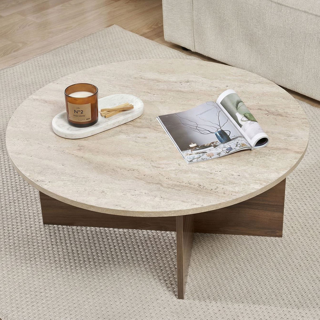 Table basse ronde avec plateau en travertin et base en bois foncé en forme de croix.