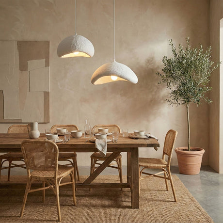 Twee crème organische hanglampen boven een houten eettafel met rieten stoelen in een serene, Japandi-stijl eetkamer.