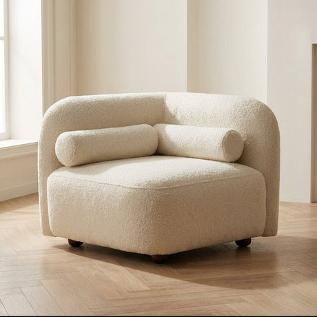 Afgeronde crème bouclé hoekfauteuil met twee cilindrische bolster-kussens en houten poten.