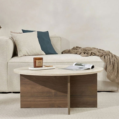 Table basse ronde avec plateau en travertin et base en bois foncé en forme de croix.